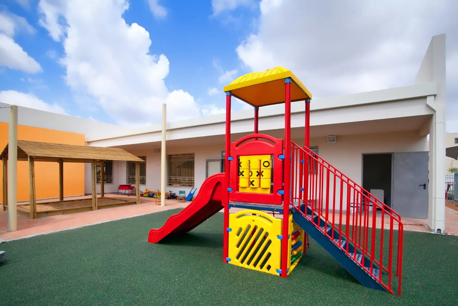 מתקן משחקים אדום וצהוב בחצר של גן ילדים